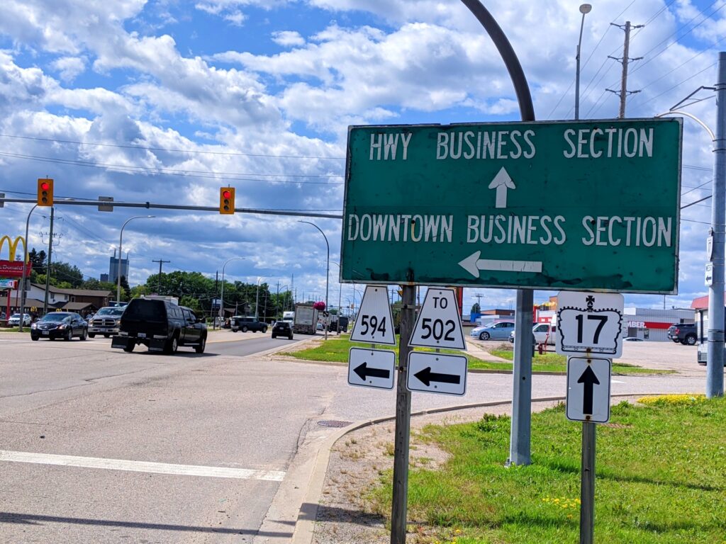 Sign next to traffic lights that reads "highway business section" with arrow pointing forwards and "downtown business section" with arrow pointing left.