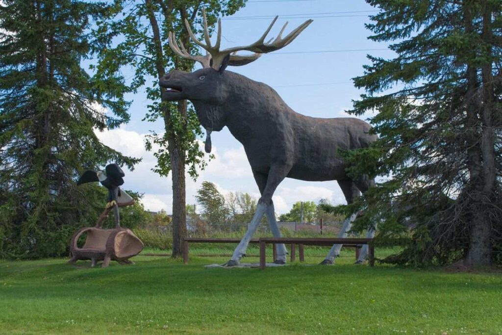 Large moose statue and eagle statue standing between two evergreen trees