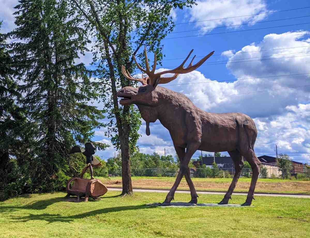 Large 18 foot moose statue standing beside 8 foot eagle statue in the grass.